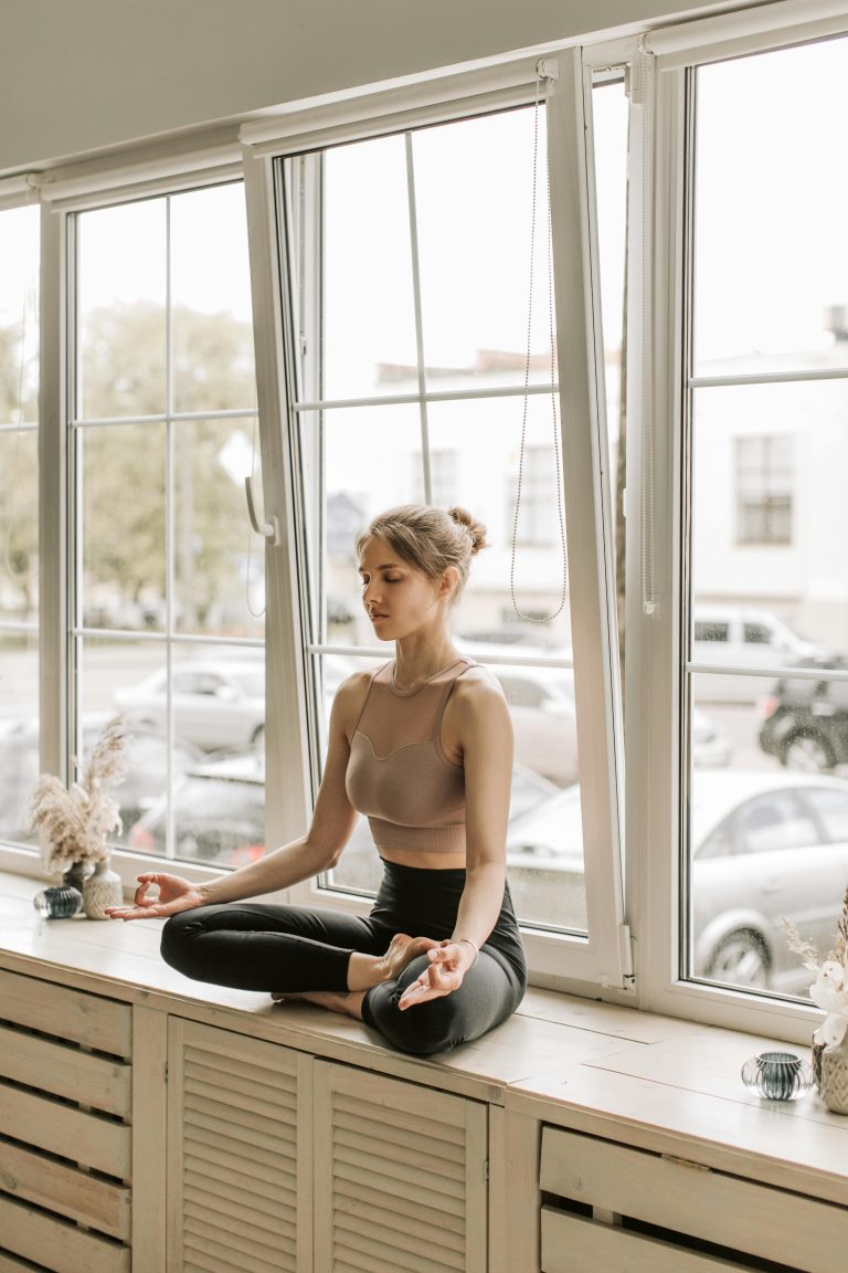 Woman meditating cross-legged on a windowsill for inner balance, demonstrating our Ayurvedic Wellness Services.