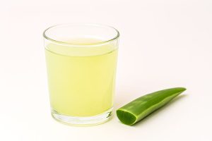 A clear glass of light green Aloe Vera juice next to a fresh, cut leaf, representing a hydrating drink often incorporated into Ayurvedic daily rituals.