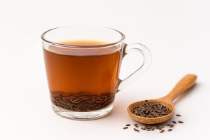 Clear glass mug of Jeera Water (Cumin Tea) showing whole seeds, used as part of Ayurvedic daily rituals for digestive health, with a spoon of cumin seeds on the side.